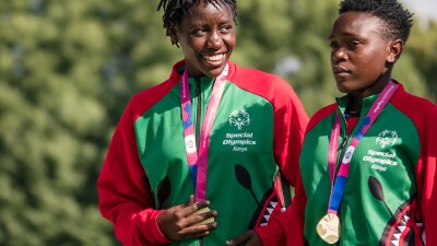 athlete smiling holding medal next to teammate 