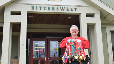 A Special Olympics athlete stands outside her group home with all of her medals and ribbons on display. 