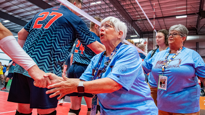 A Special Olympics coach shakes hands with athletes on the other side of a volleyball net. 