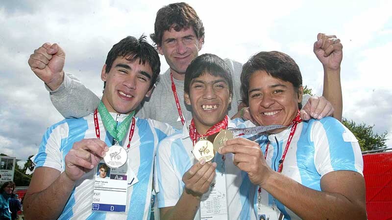 3 athletes in the front row are showing off their medals, another athlete stand behind them fist pumping for victgory.