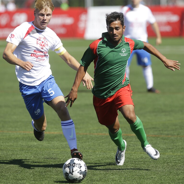 Two male athletes on the pitch going for the ball. 