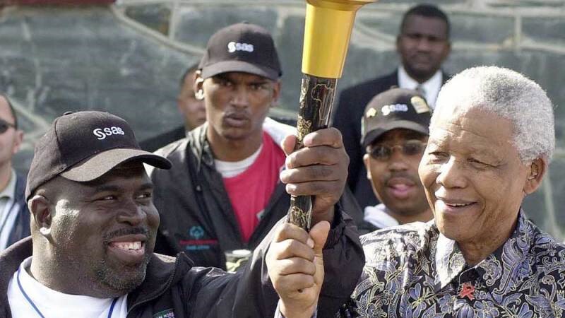 Two men holding the Flame of Hope with five spectators in the background. 