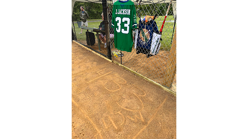 A green softball jersey hangs on the fence. "433" is written in the dirt below it. 