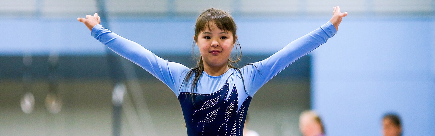 Young girl in a blue leotard raising her arms as she finishes her routine. 