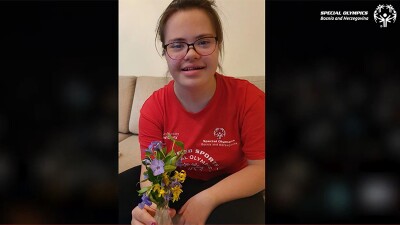 Athlete, Edna Sunjic, smiling, sitting on a couch, and holding flowers. 