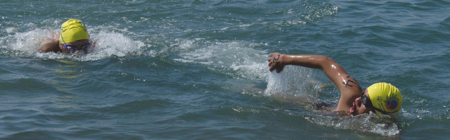 Two athletes with yellow caps swimming in the water. 