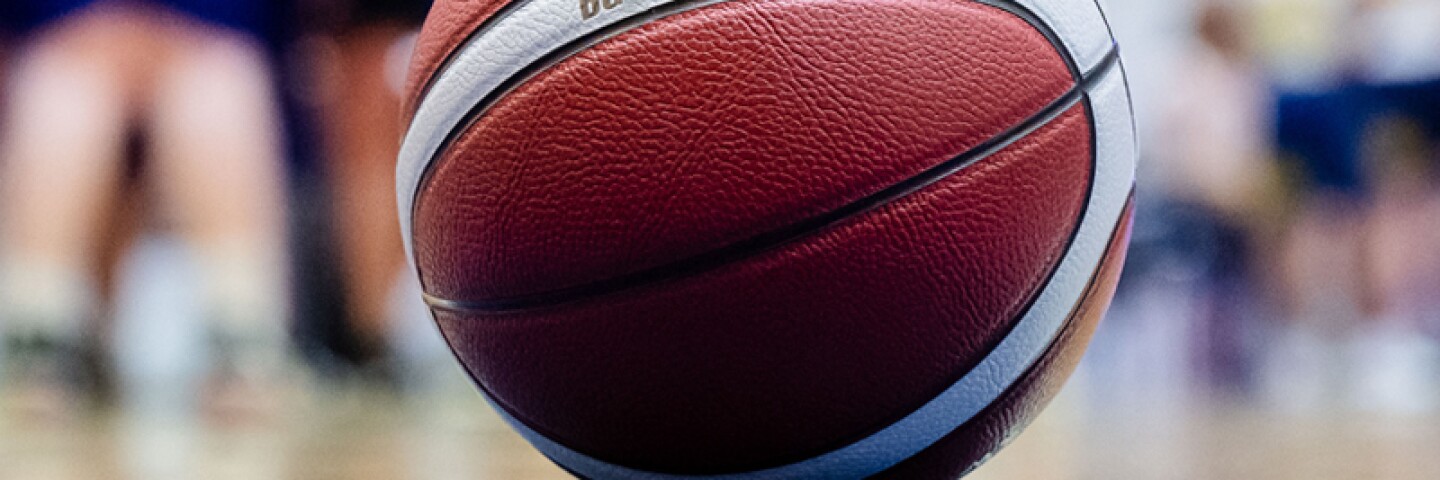 A basketball sitting on the court and the team is in the background. 