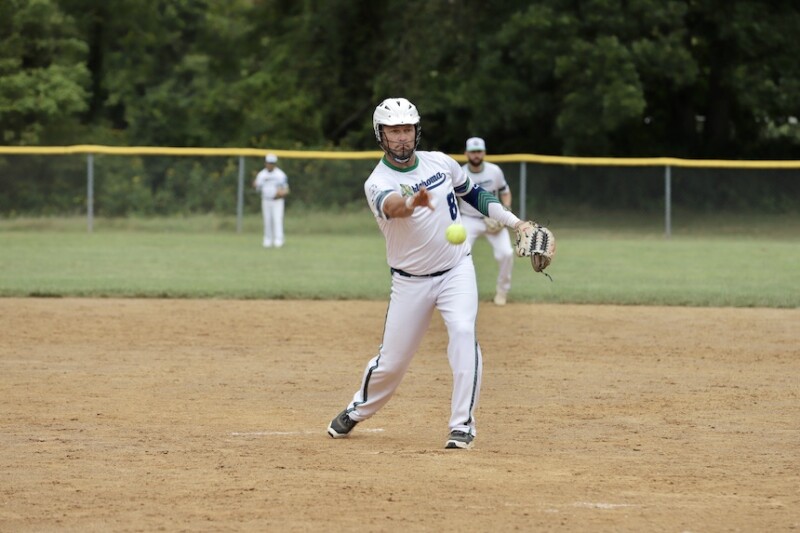 A pitcher stands on the pitcher's mound in a softball field. He's throwing the ball. 