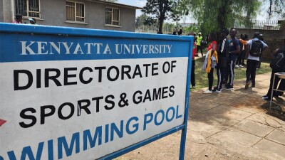 Kenya University swimming sign in the foreground with a large group of people waiting at the entrance.