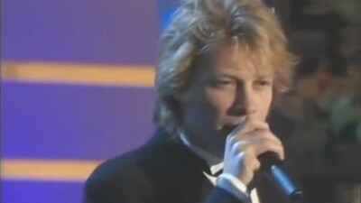 Jon Bon Jovi dressed up in a tuxedo singing on stage. 