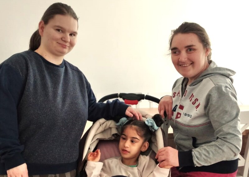 Olek and Vita stand posing for the camera with Rosa sitting in a stroller between them.