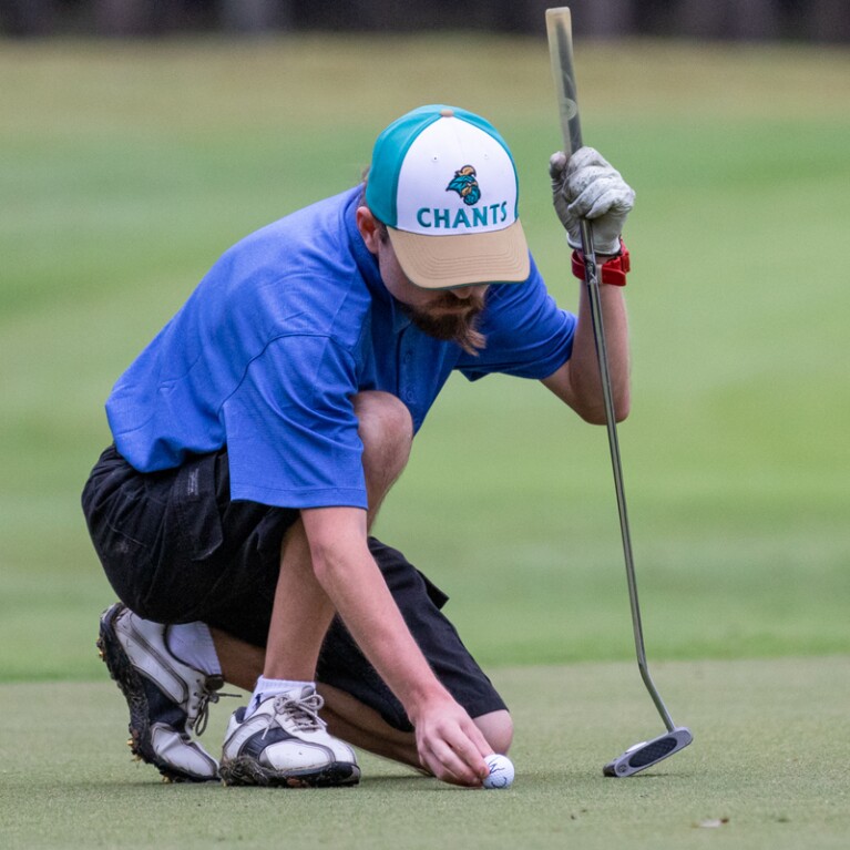 Golfer kneeling down to adjust his ball. 