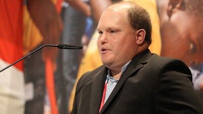 Close up of Ben Haack, in a suit jacket, speaking into a microphone.