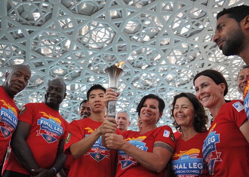 A group of people standing in a semi-circle wearing Final Leg Law Enforcement Torch Run t-shirts and holding the Flame of Hope. 