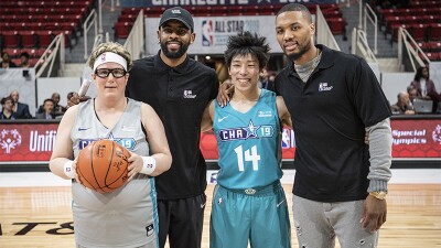 Two NBA players standing behind two Special Olympics athletes on the court. 