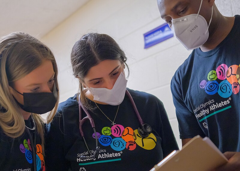 Three people wearing Healthy Athletes branded t-shirts and looking over a paper on a clipboard. 