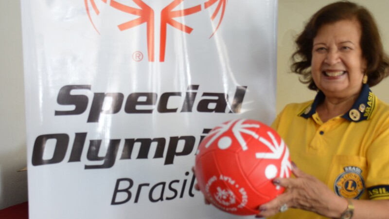 Woman smiling and posing with a red football (soccer ball) standing next to Special Olympics Brazil signage. 