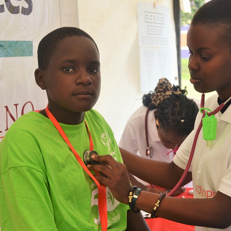 A female health care professional is listening to an athletes heartbeat with a stethoscope. 