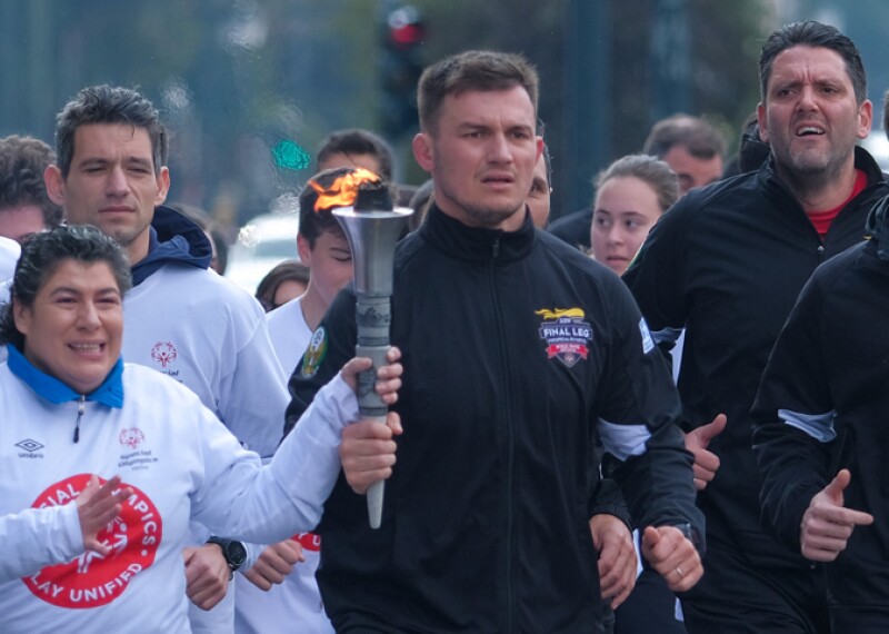 Athletes and Law Enforcement Torch Run officers running together; an athlete is holding the Flame of Hope. 