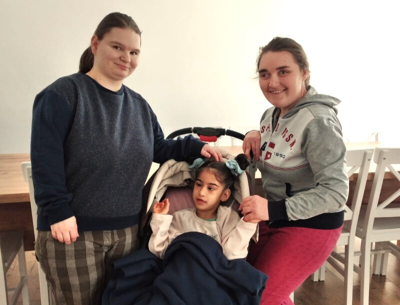 Olek and Vita stand posing for the camera with Rosa sitting in a stroller between them.