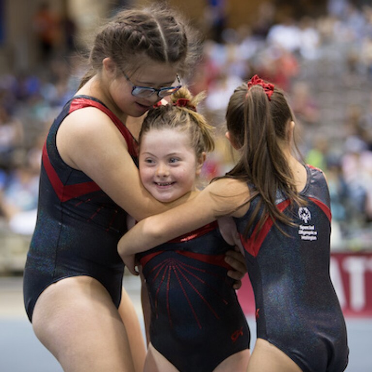 Three young female gymnasts hugging one another. 