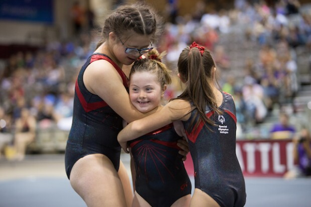 Three young female gymnasts hugging one another. 