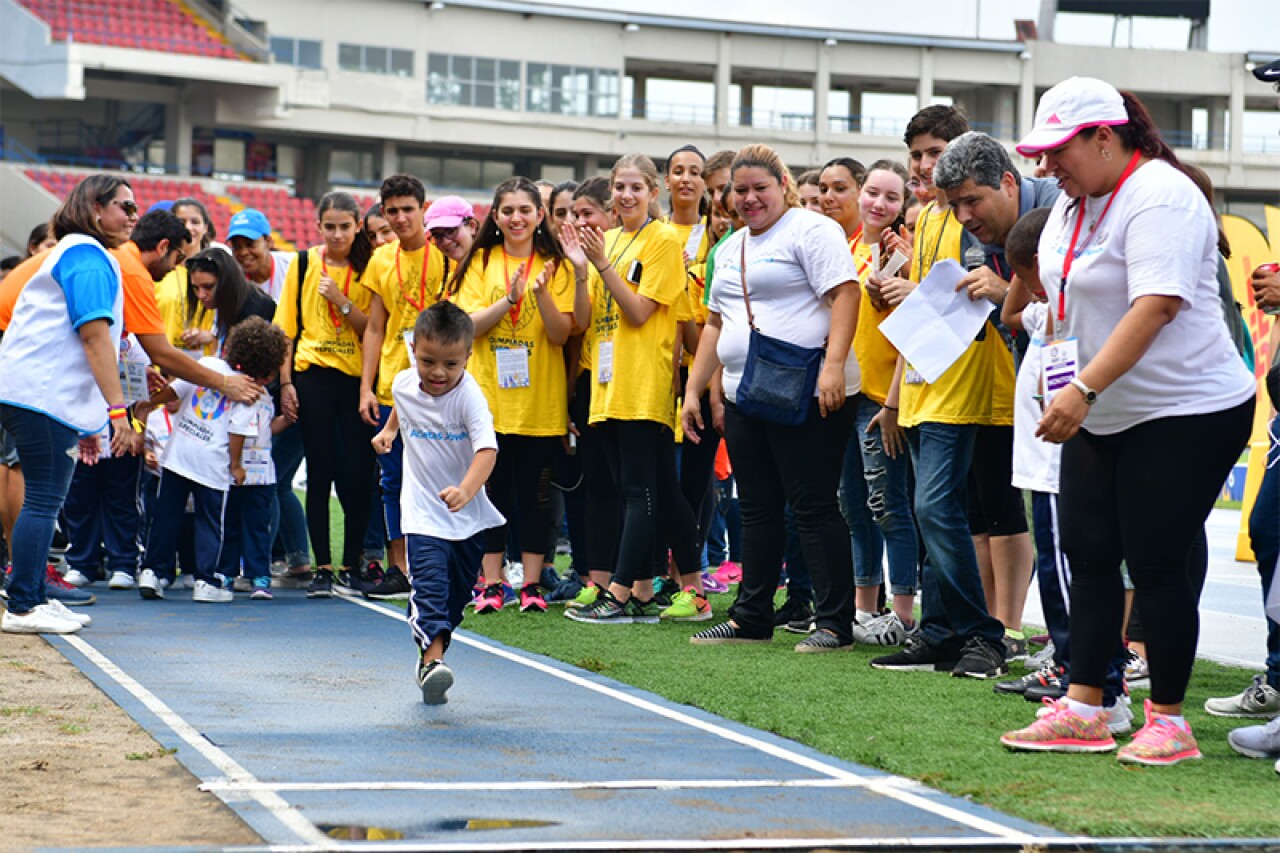 Young athlete runs while adults cheer him on.