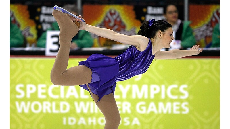 Figure skater balancing on one blade with the other leg lifted and holding onto the blade. 