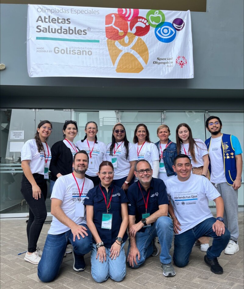 Group of 12 people smiling and posing for the camera with a Healthy Athletes banner hanging in the background.