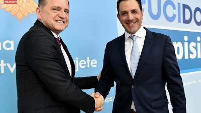 Two men wearing suits, shake hands and smile at the camera