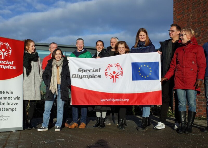 Eleven people holding a Special Olympics and European Union branded flag. 