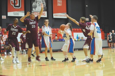 A female player prepares to shoot the ball while males players on the other team attempt to block. 