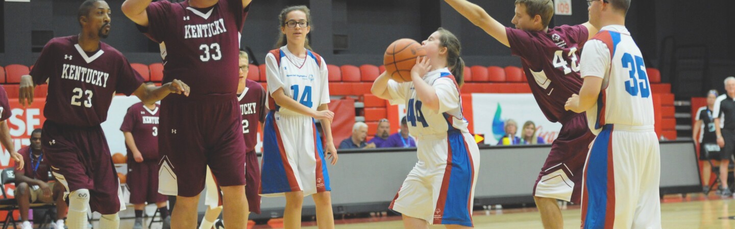 A female player prepares to shoot the ball while males players on the other team attempt to block. 