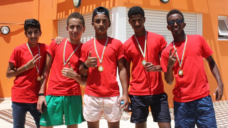 Five athletes in red shirts standing side by side with medals around their necks. 