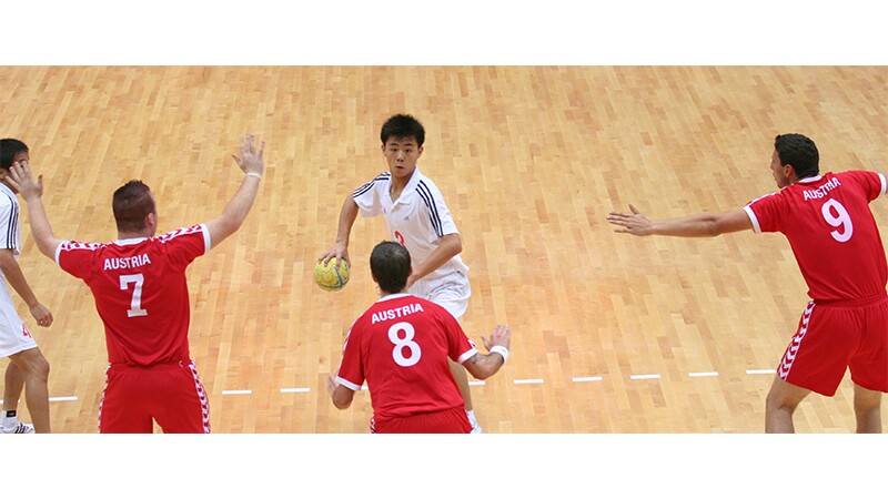 Two young men in white playing three young men in red in a game of handball.