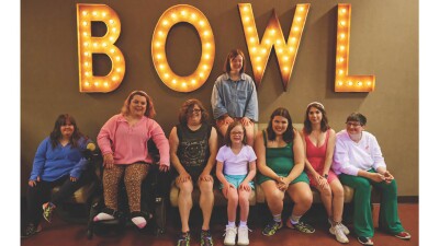 Group of 8 young women sitting on a couch under a sign that reads, "Bowl." 