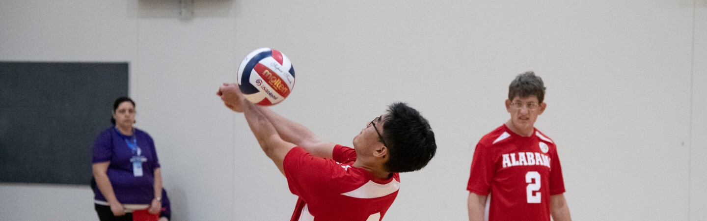 Male athlete hitting the ball while his teammate and official watch. 