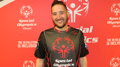 A man stands in front of a red background and smiles for a photo. 