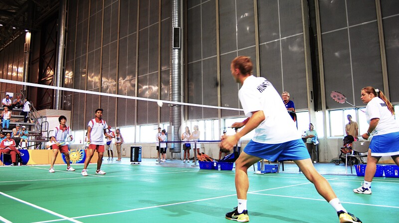 A player swings at the birdie as his teammate and the opposing team watches. 