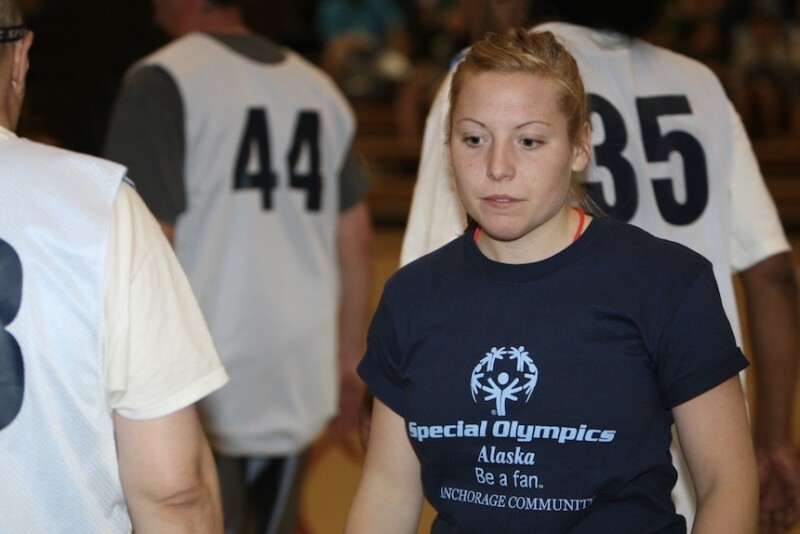 A woman wearing a Special Olympics Alaska t-shirt high fives someone wearing a basketball jersey. 