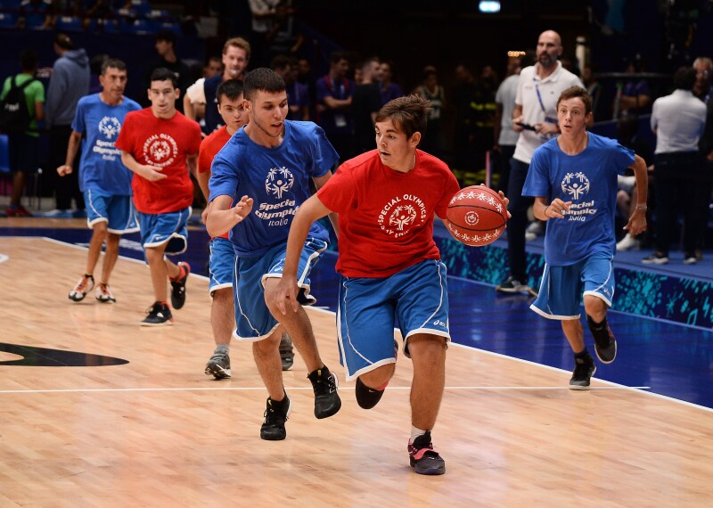 Three players with blue jerseys and 3 with red jerseys run on an indoor basketball court