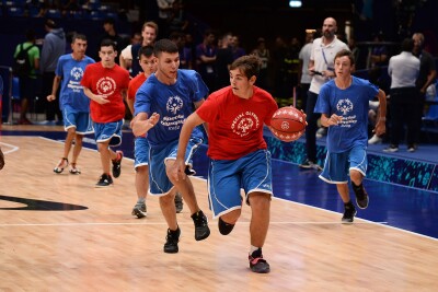 Three players with blue jerseys and 3 with red jerseys run on an indoor basketball court