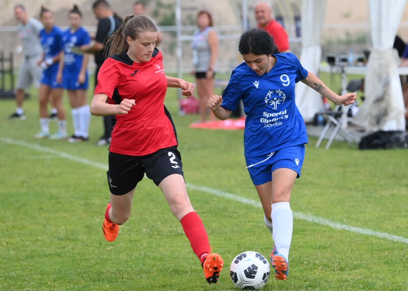 Two girls on the pitch kicking the ball. 