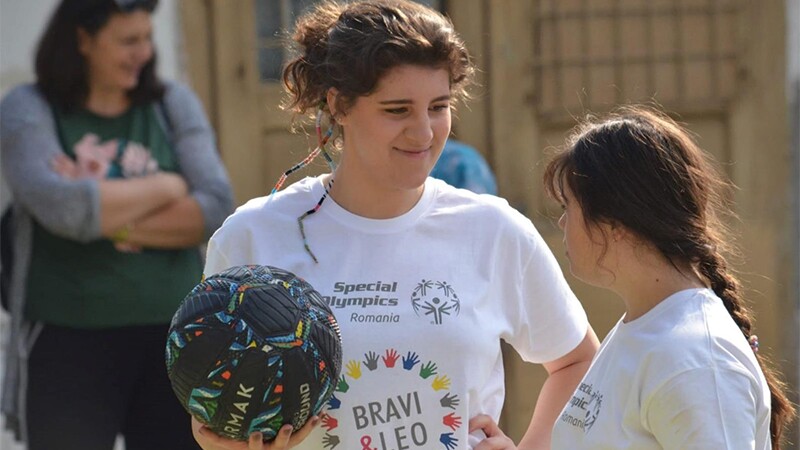 A young woman holding football (soccer ball) talking with an athlete on the field. 