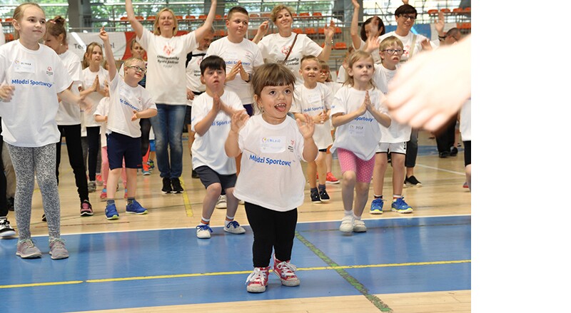 Young and Unified athletes and volunteers in a gymnasium warming up. A young female athlete is in the foreground. 