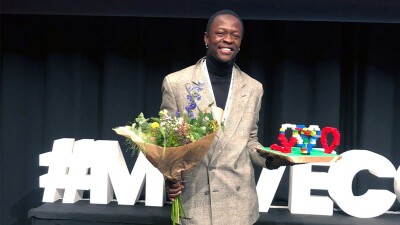 Gerald Mballe holding flowers and an award. 