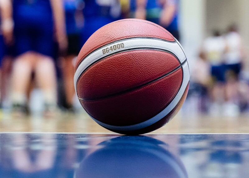 A basketball sitting on the court and the team is in the background. 