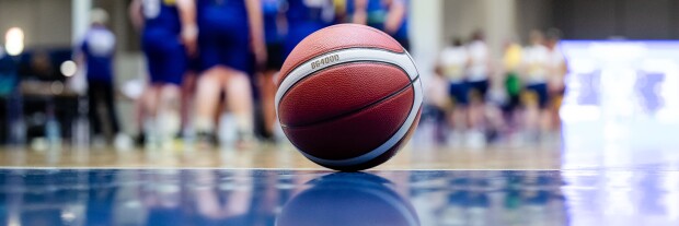 A basketball sitting on the court and the team is in the background. 