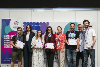 Group of eight people smile into the camera; notably among them the four Young Reporters who display their certificates.