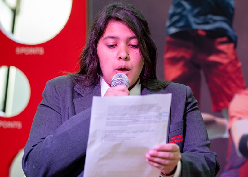 Young woman reading from a script and speaking on stage. 